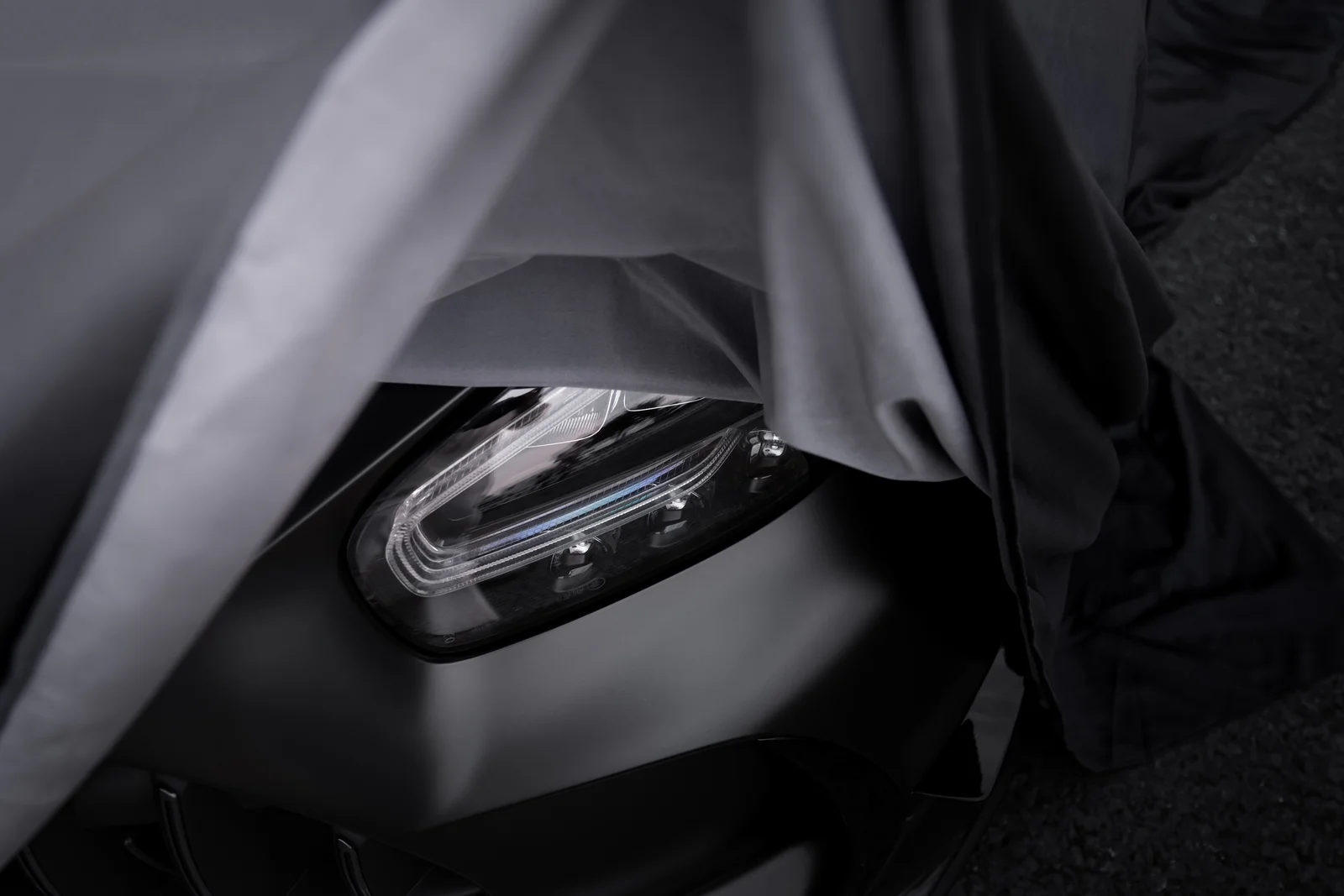 Headlight revealed beneath a partially lifted car cover