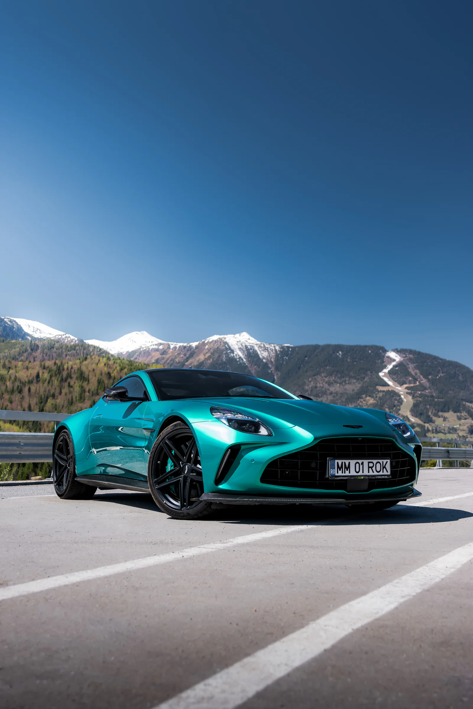 Front three-quarter view of the turquoise Vantage beneath a clear sky and snowy mountains