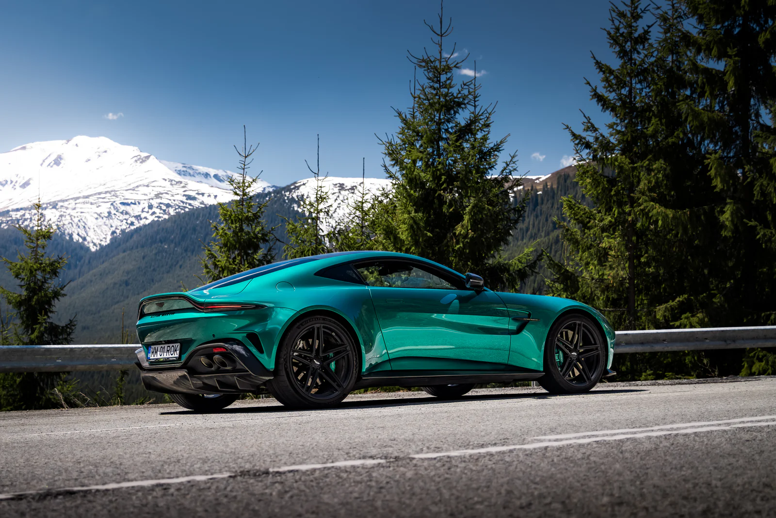 Rear three-quarter view of the turquoise Vantage on a sunlit mountain road