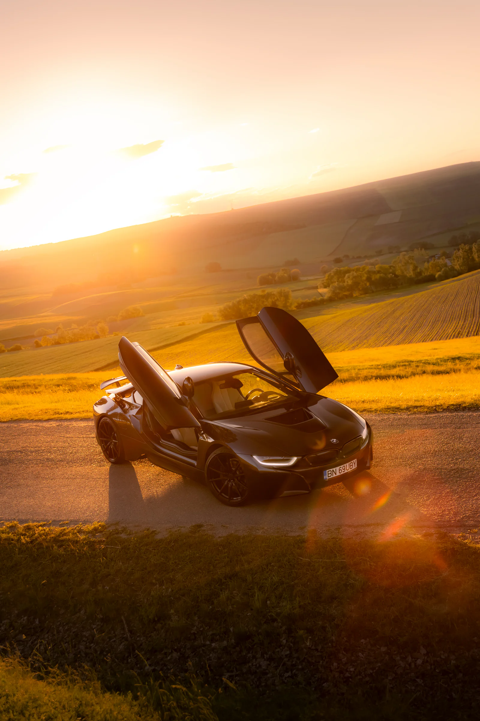 Elevated portrait of the BMW i8 with raised doors above the sunset valley