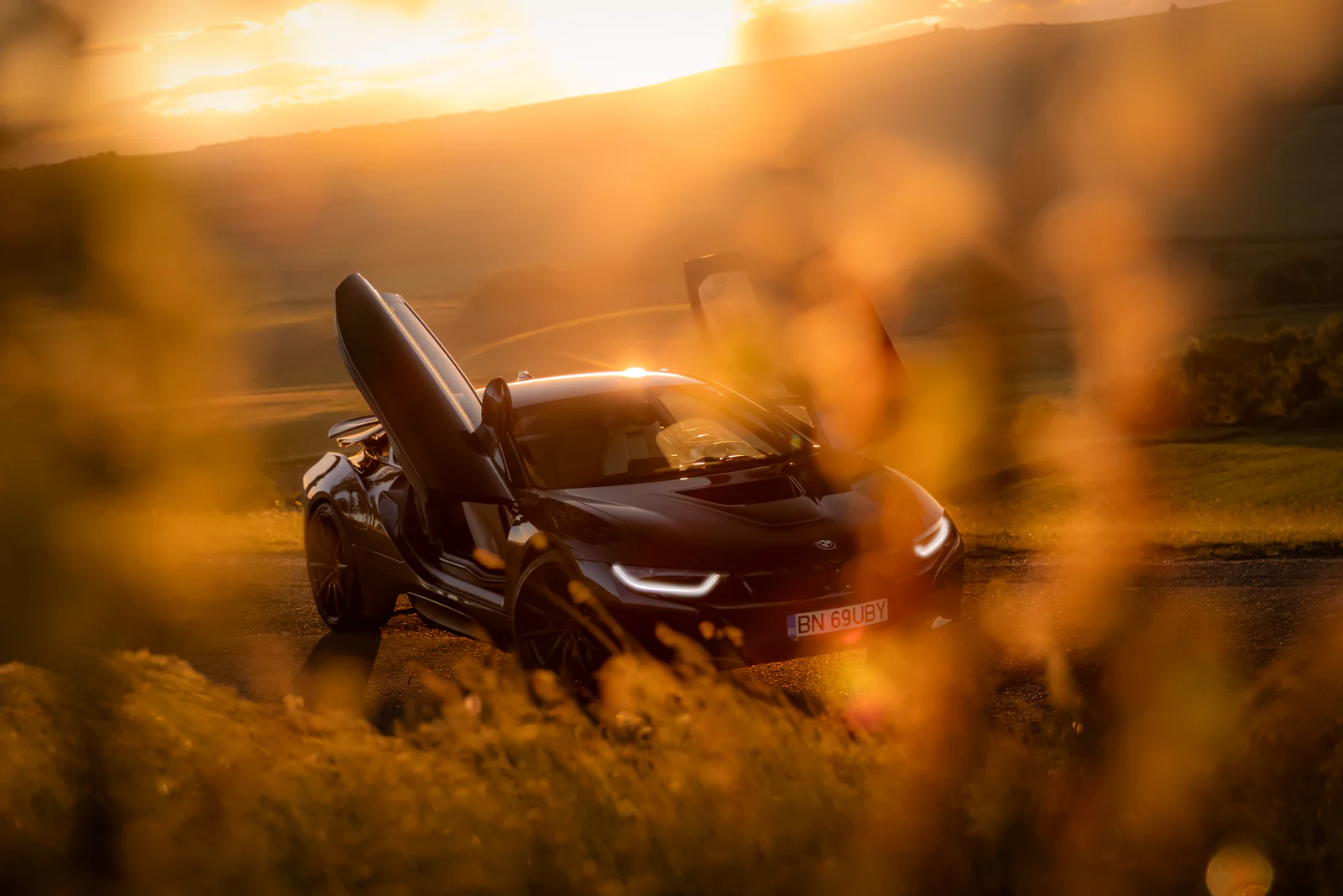 BMW i8 with butterfly doors raised, framed through golden foreground grass
