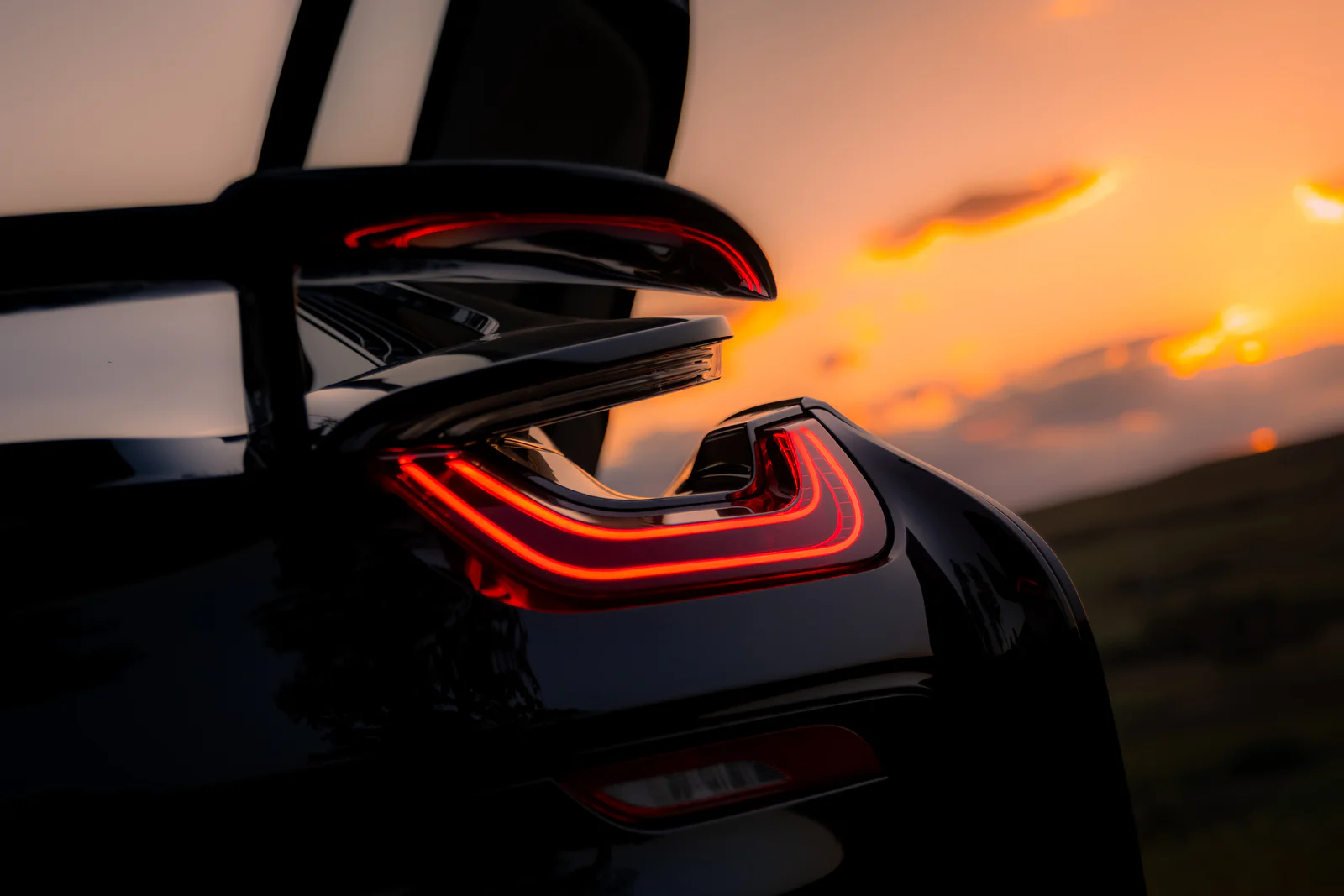 Sharp red rear light and sculpted body against a softly focused orange sunset