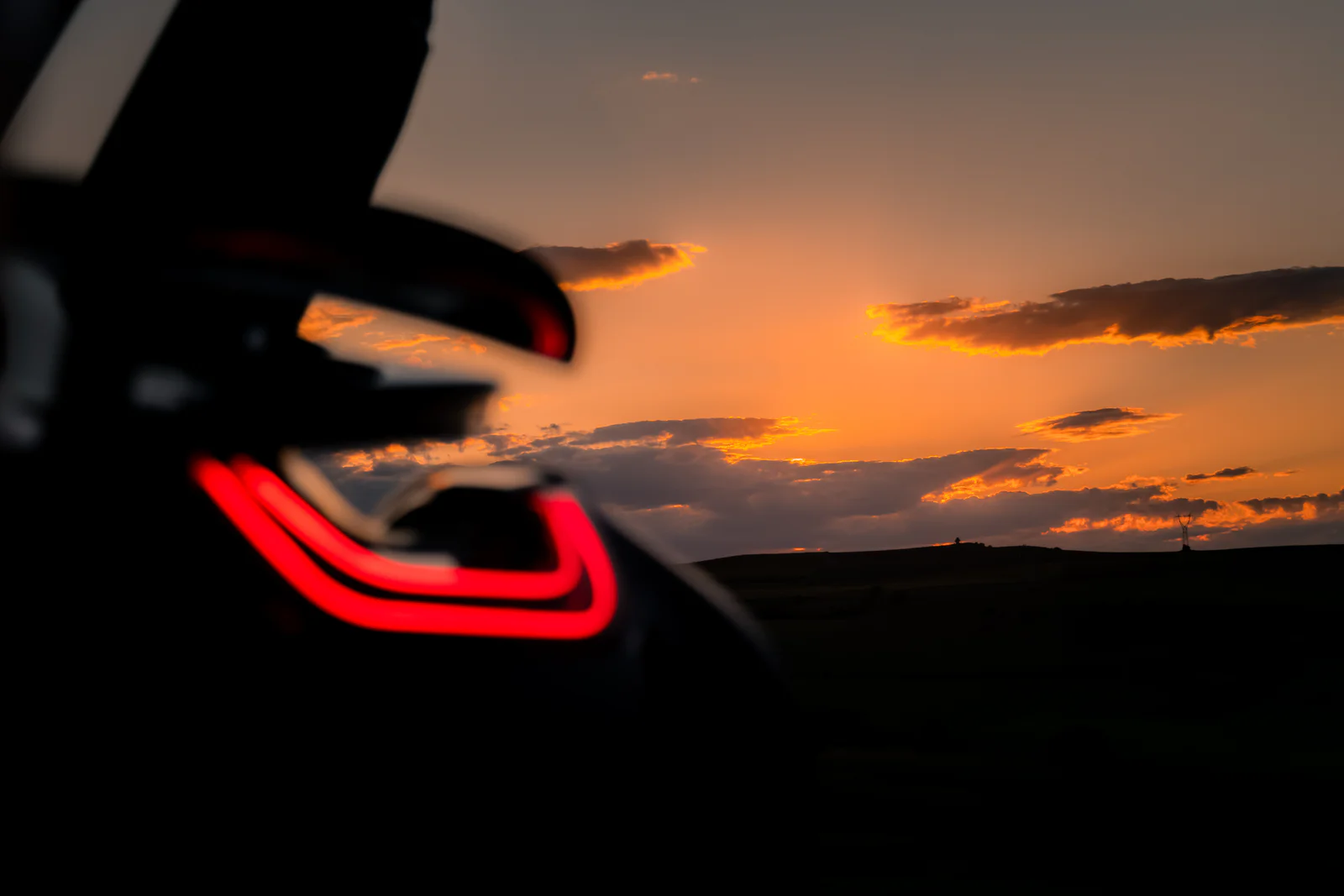 Softly focused red rear light framing sharp orange sunset clouds