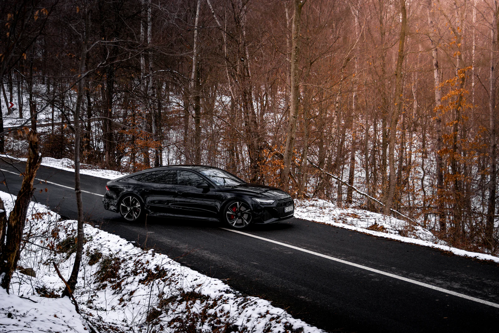 Black Audi RS7 on a winding road through the winter forest