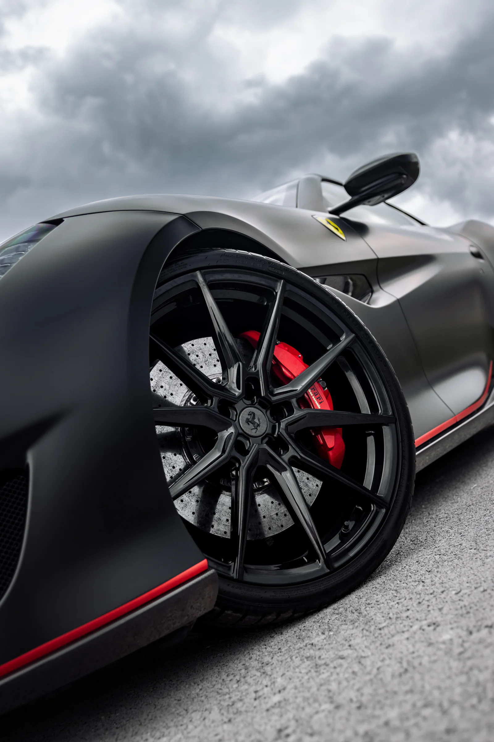Low-angle detail of the black alloy wheel and red Ferrari brake caliper