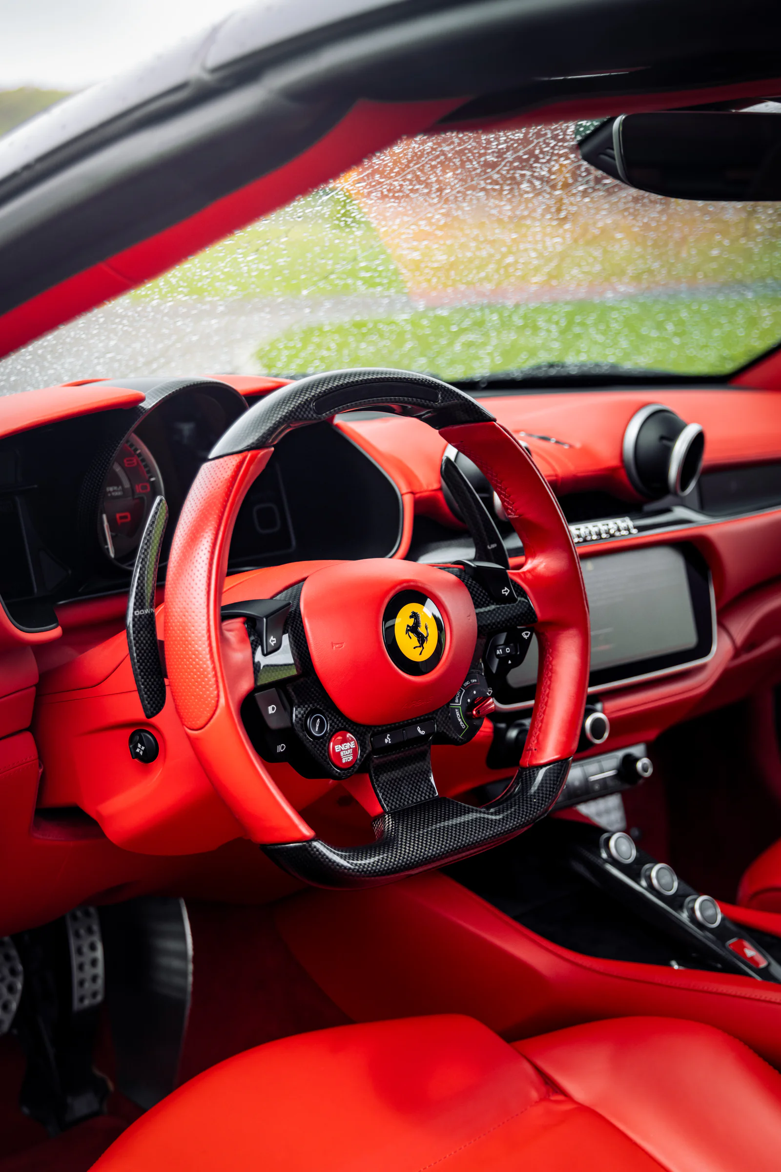 Red leather Ferrari steering wheel with rain on the windscreen