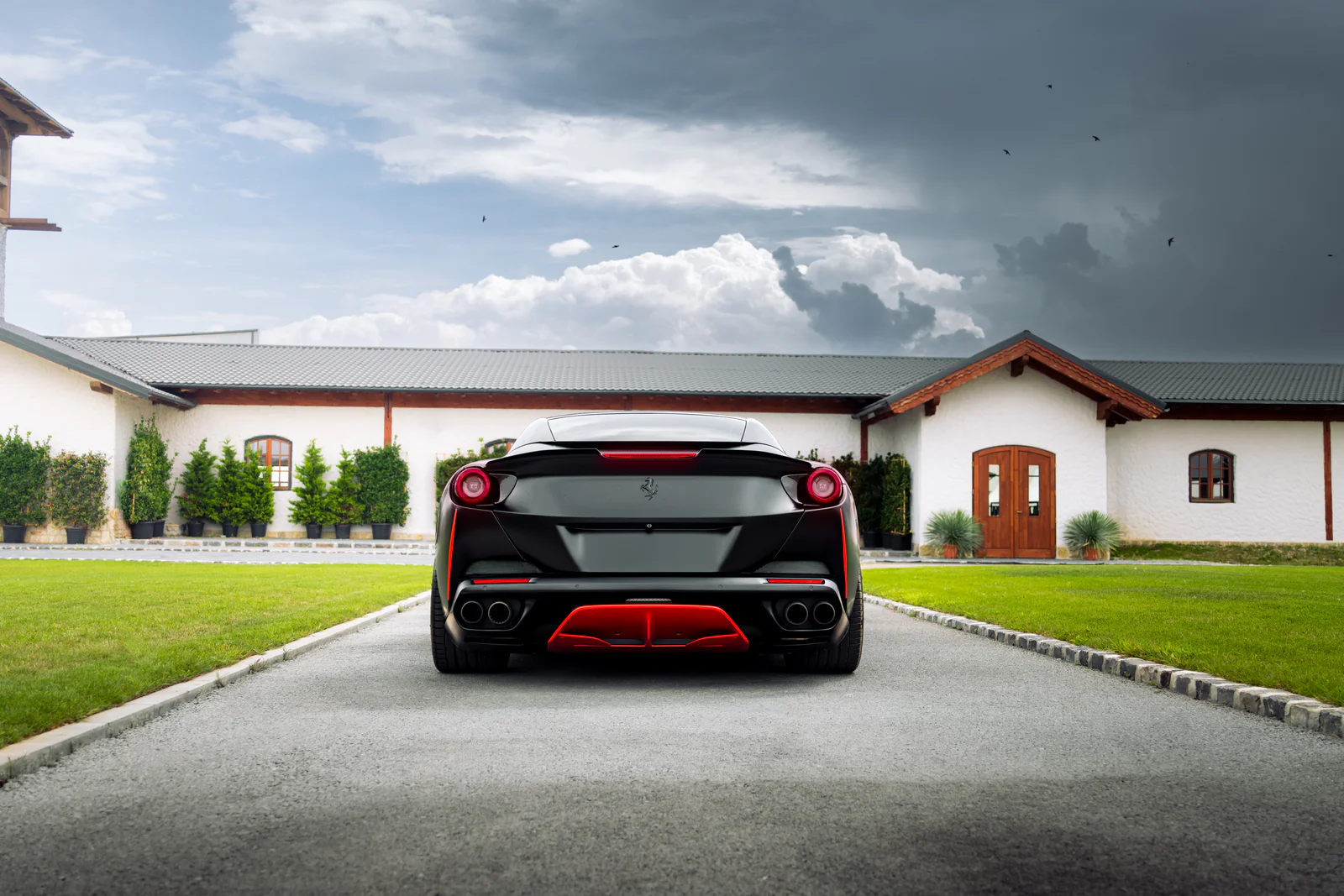 Wide rear view of the matte black Portofino in front of white courtyard buildings