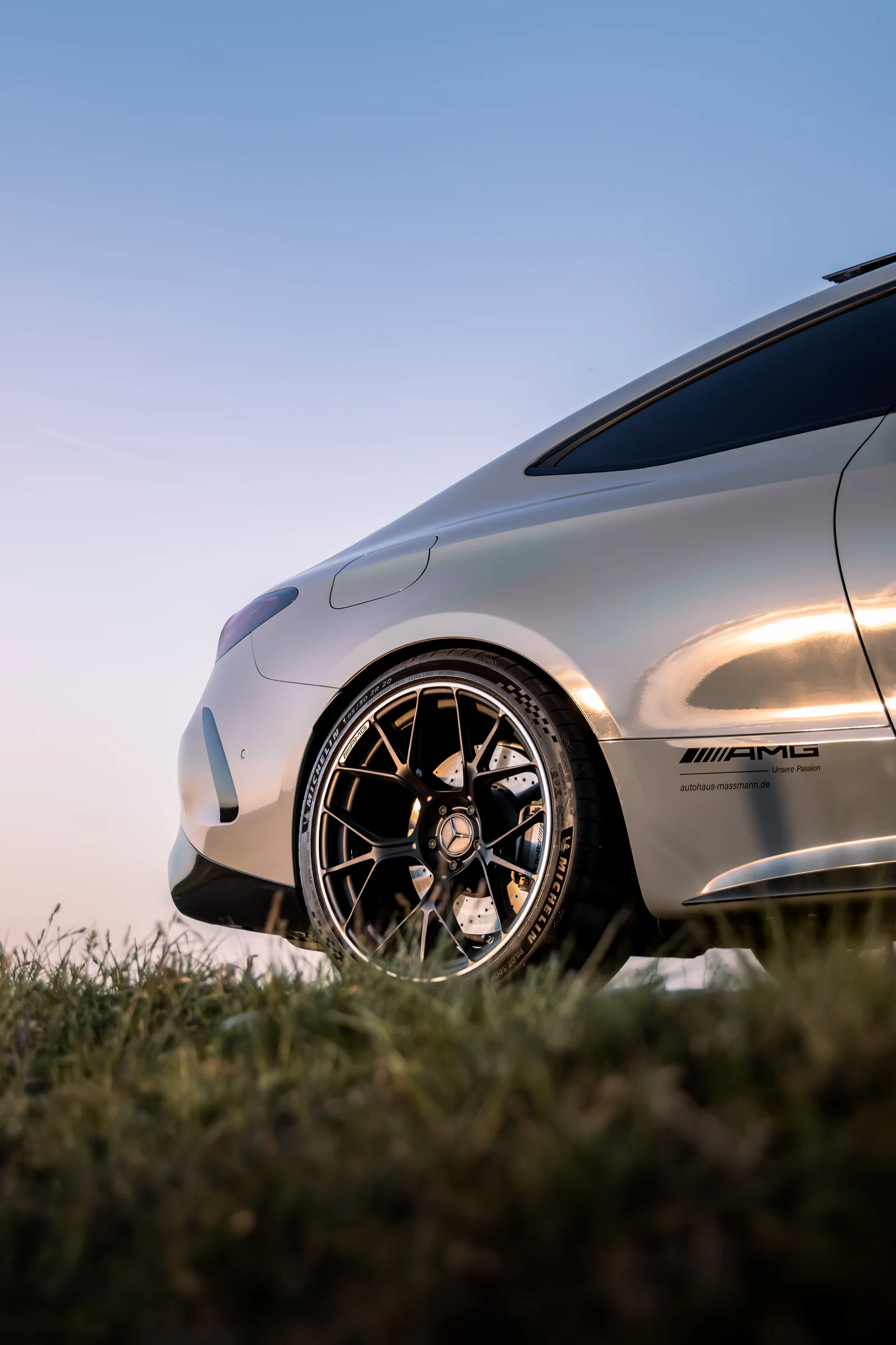 Rear wheel and coupe body catching the sunset above foreground grass