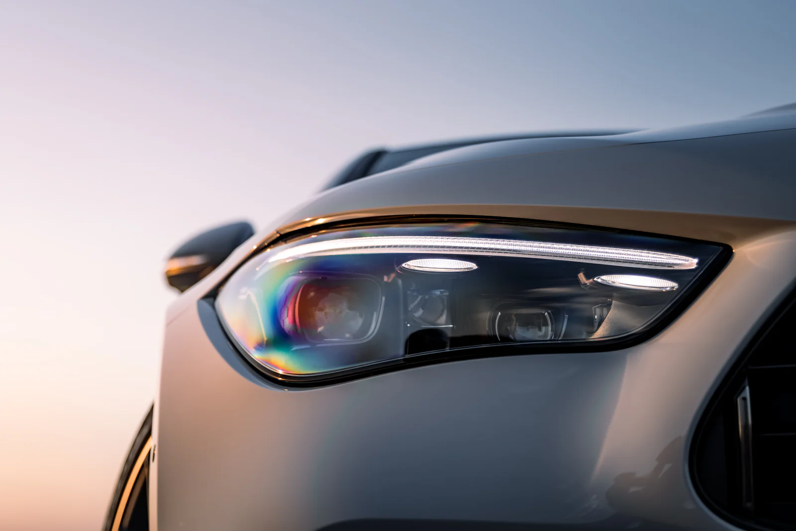 Headlight lens reflecting rainbow colours and the evening sky