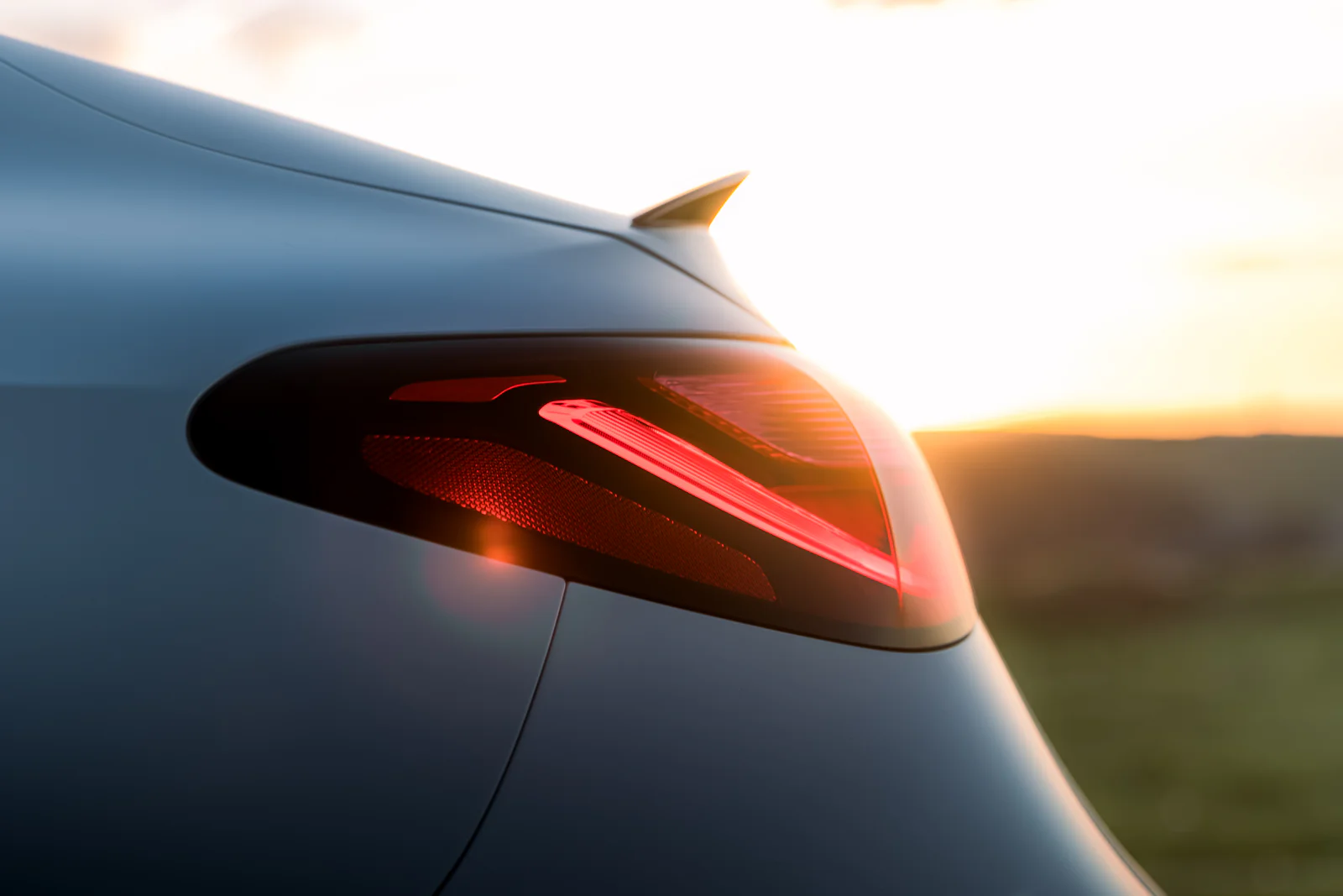 Illuminated red taillight beside the setting sun