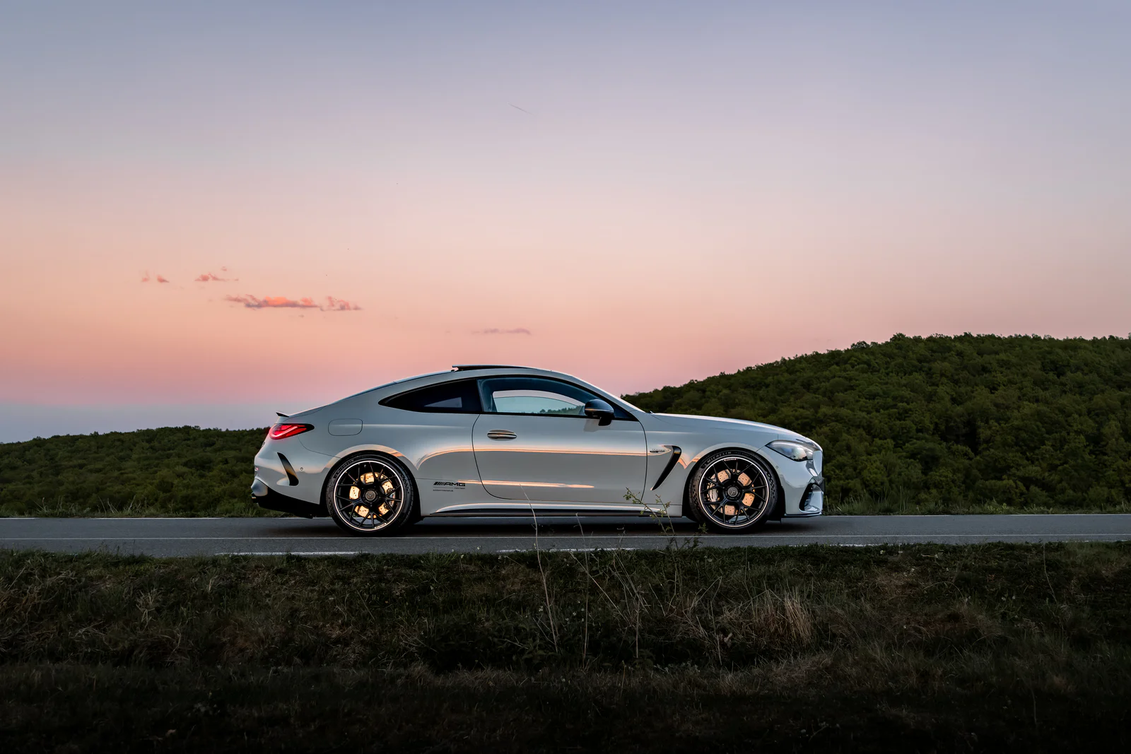 Full coupe side profile against a pink sky and wooded hills